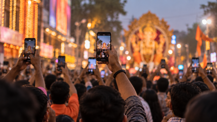 Dense Indian festival crowd with several arms raised holding phones above the heads in evening light