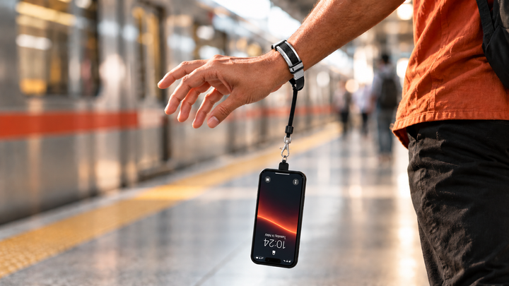 Phone hanging upside down from a phone bracelet on a railway platform, held safely on the wrist