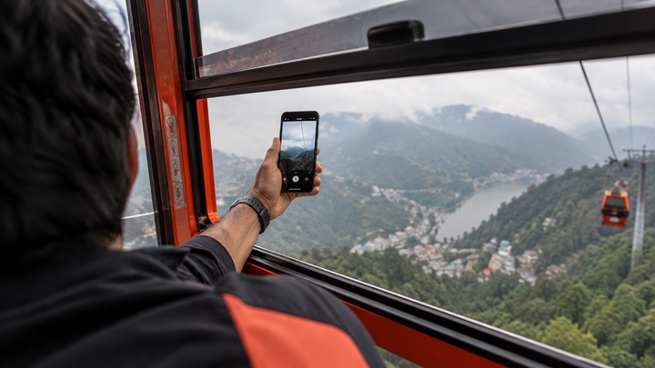 Hand holding a phone out over a railing at a high Indian viewpoint with a long drop below